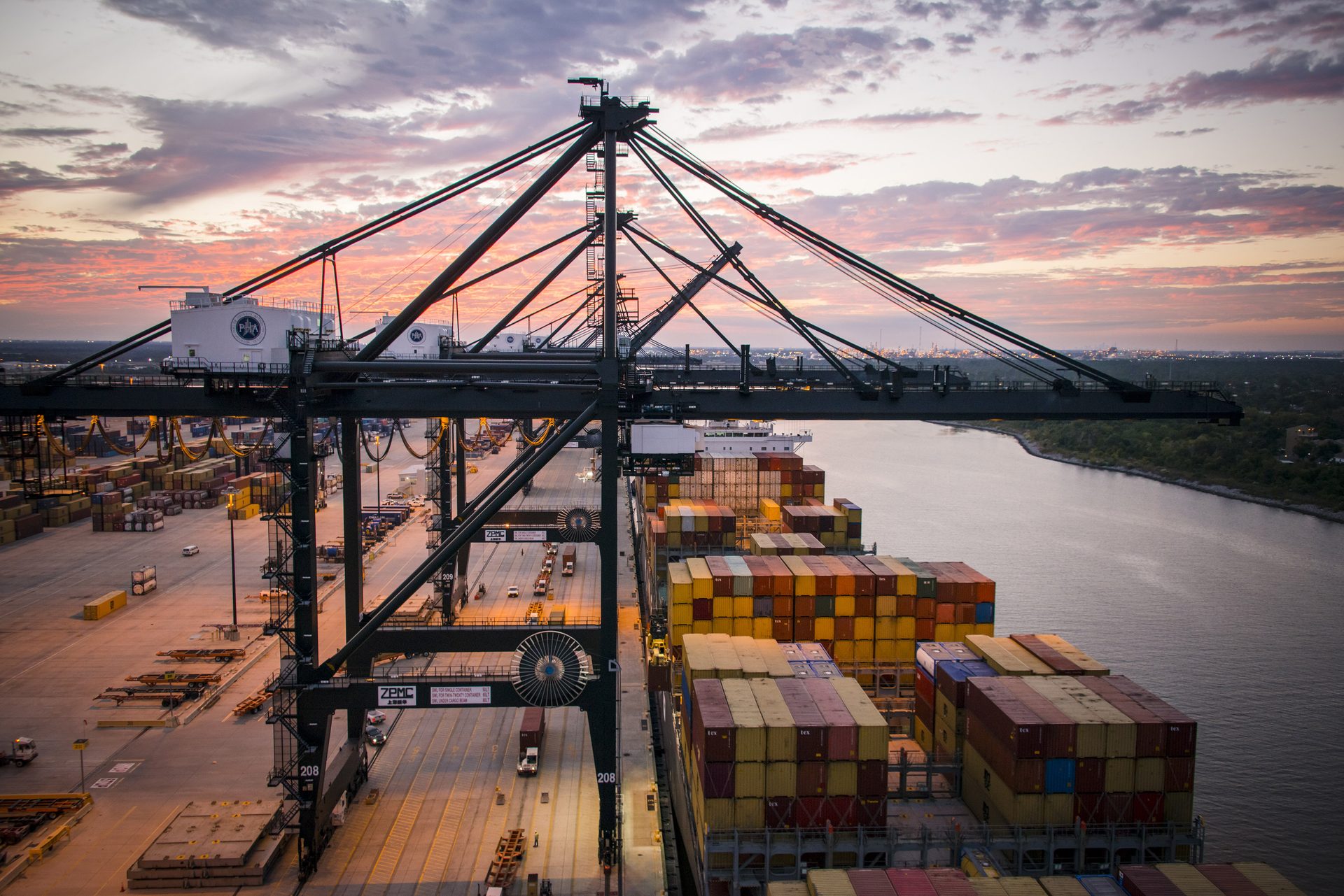 A gantry crane loading colorful shipping containers onto a vessel at the Port of Houston at sunset.